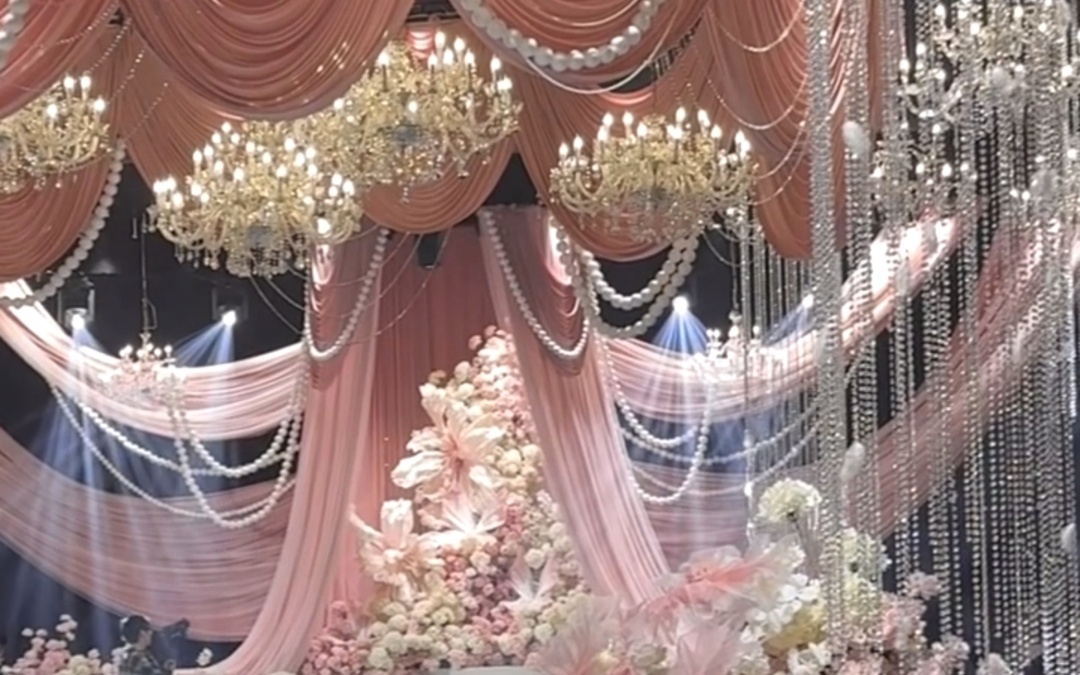 粉调布幔铺陈，珍珠链点缀，水晶灯摇曳，鲜花装点浪漫现场