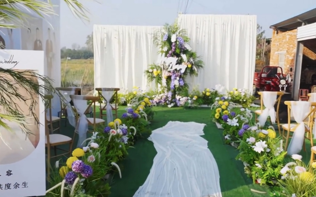 纯白布幔轻扬，绿茵草坪映衬鲜花立柱